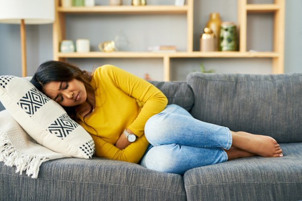 Shot of a young woman suffering from stomach cramps at home