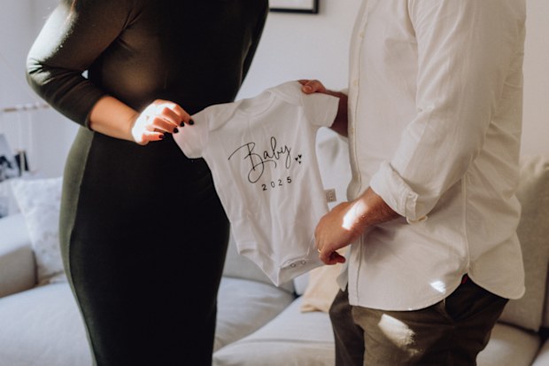 A heartwarming photo of a couple holding a baby bodysuit with 'Baby 2025' written on it, symbolizing their excitement and love as they prepare for the arrival of their new baby. This image celebrates family, milestones, and the journey to parenthood.