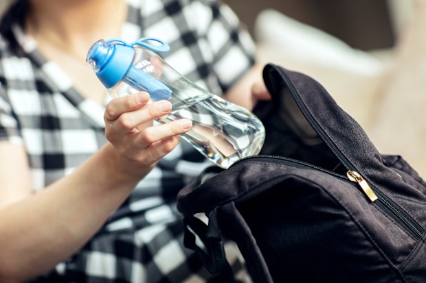 Woman takes the bottle out from backpack. Woman takes the reusable bottle of fresh water with carbon filter out from her backpack.