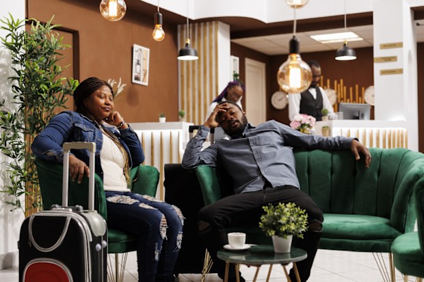 Exhausted tourists resting in hotel lobby, waiting for check-in, sleeping after long day of traveling. Tired African American couple of travelers fall asleep, taking nap, adapting to new time zone