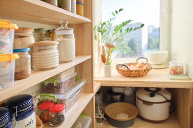 Wooden shelves with food and utensils, kitchen appliances in the pantry.