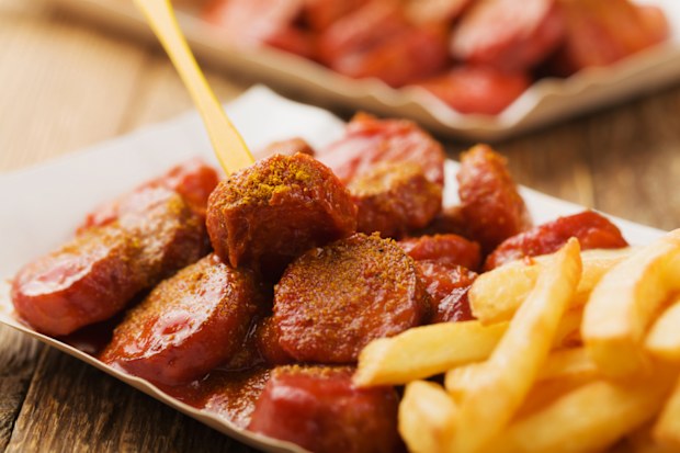 Traditional German currywurst, served with chips on disposable paper tray. Wooden table as  background.