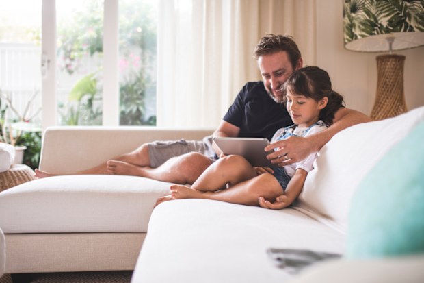 Father and daughter sitting on a sofa and using digital tablet.