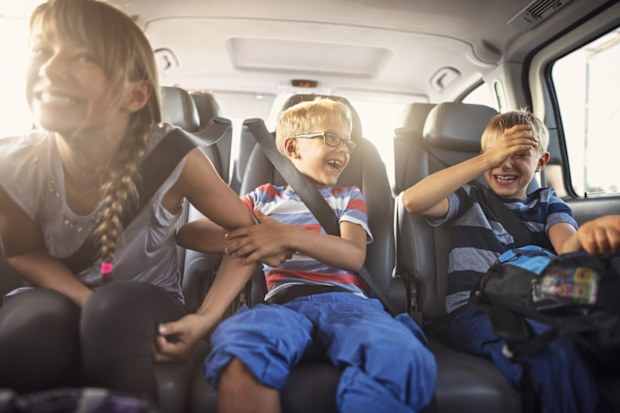 Three kids laughing in car on a road trip. Kids are aged 11 and 8. The kids are laughing and playing. Sunny summer day. Nikon D810.