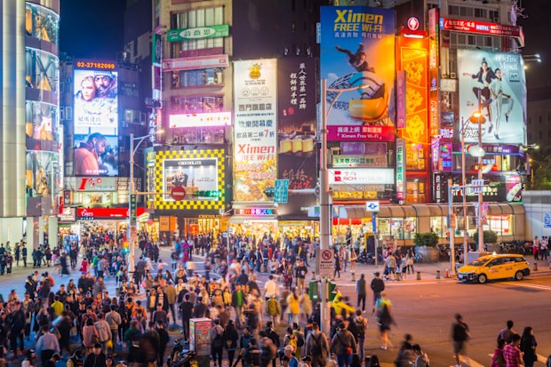 View across the crowded crossroads of Ximending past zooming traffic, shoppers and tourists enjoying the warm night illuminated by the colourful billboards and neon lights of Taipeis downtown commercial district