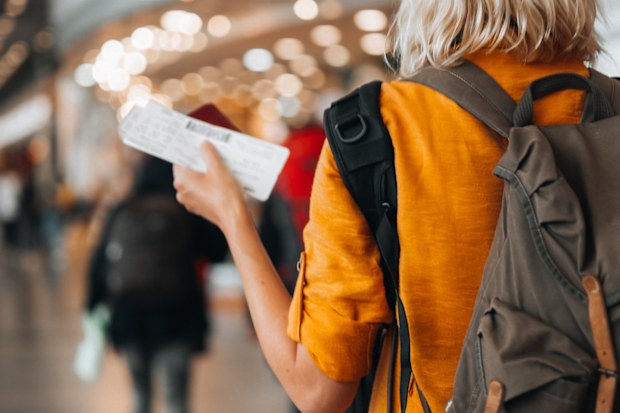 Rear view of a  woman at the airport holding a passport with a boarding pass as she walks to her departure gate