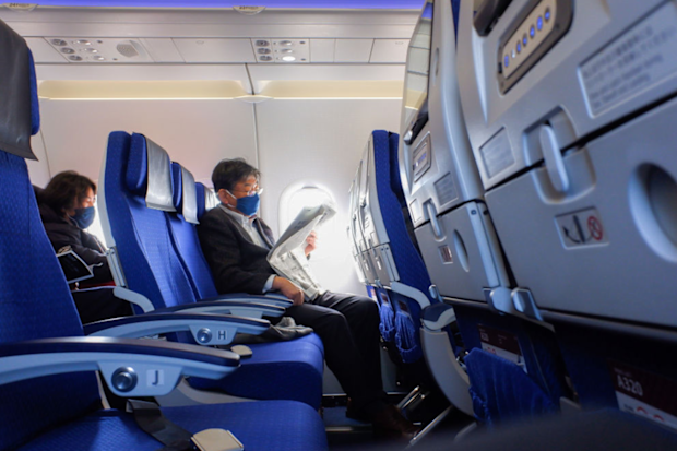 A passenger wearing a face mask seen reading a news paper inside the ANA plane