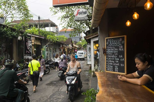 Ubud, Bali - February 12, 2017: Pedestrians and people on scooters move down a street lined with shops and restaurants in Ubud, Bali.