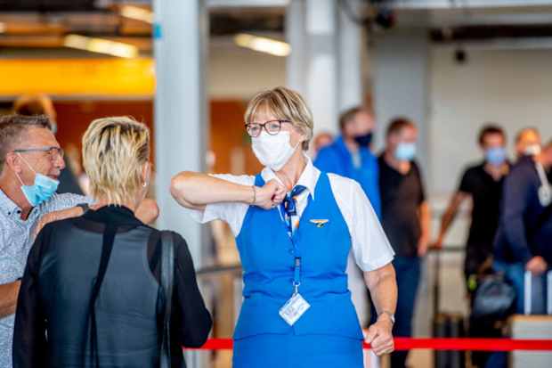 A KLM staff doing the elbow bump with travellers while wearing a face mask