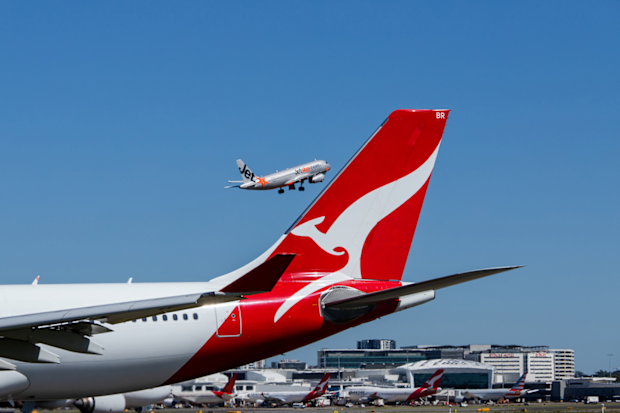 Qantas aircraft on tarmac and Jetstar plane flying in the background
