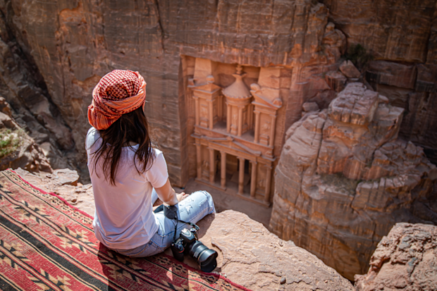 Woman sits and views Petra, Jordan from cliff