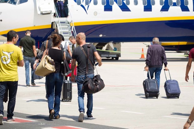 Passengers walking with carry-on luggage toward a Ryanair plane. 