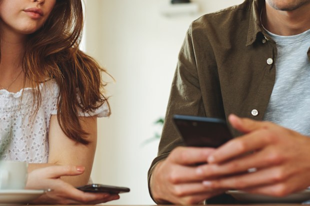 Woman looking unhappy while her man paying no attention to her and busy using his mobile phone. Sulking woman sitting next to man reading text messages during a date.
