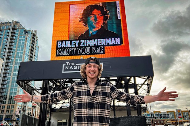 Bailey Zimmerman poses in front of a Billboard promoting his single.
