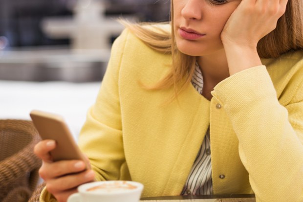Lonely woman looking at her mobile phone while sitting at the cafe.