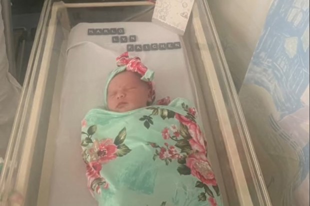 Newborn baby wrapped in floral blanket lying in bassinet at the hospital.