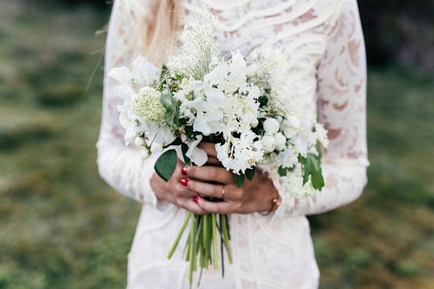 Bride standing in white dress holding flowers.
