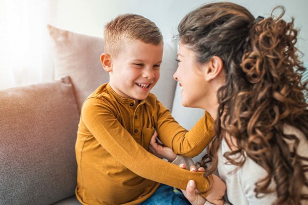 A mother and son sitting on a couch and smiling at each other.