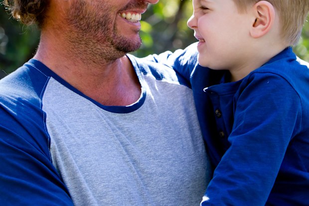 Father holding young son outdoors in sunlight in park - looking away from camera
