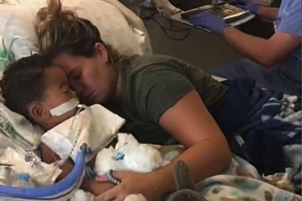 Mum hugging son lying in hospital bed.