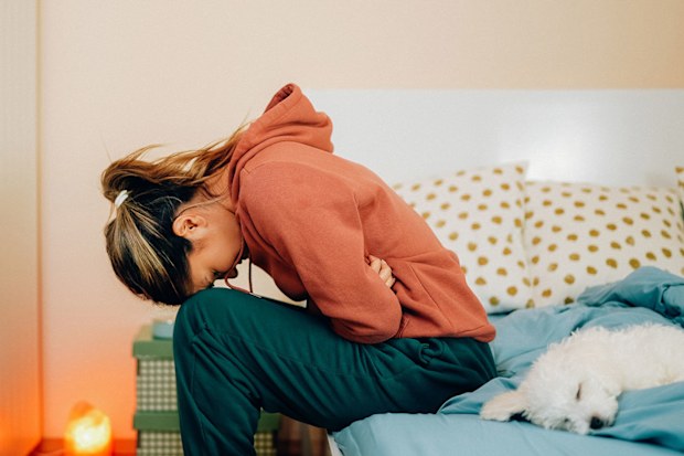 Young woman in pain sitting on her bed.