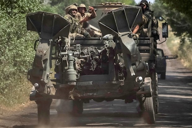 Ukrainian servicemen ride on a military vehicle as they tow an M777 howitzer near the front line, in the Donbas region.