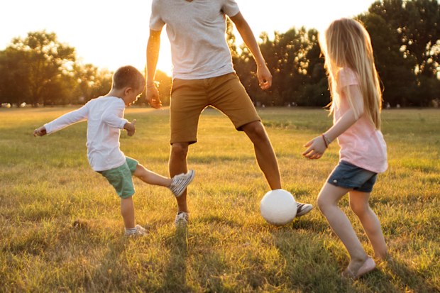 Kids and father playing soccer on a beautiful summer afternoon outdoors