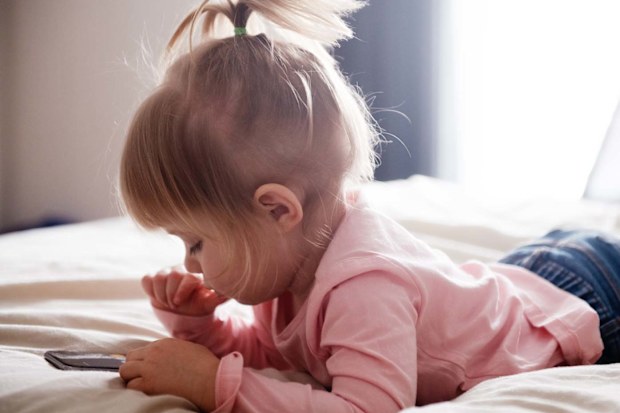 Toddler using a phone while lying on her stomach in bed