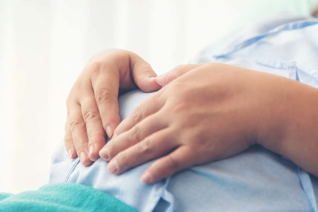 Pregnant woman lying in hospital holding her stomach.