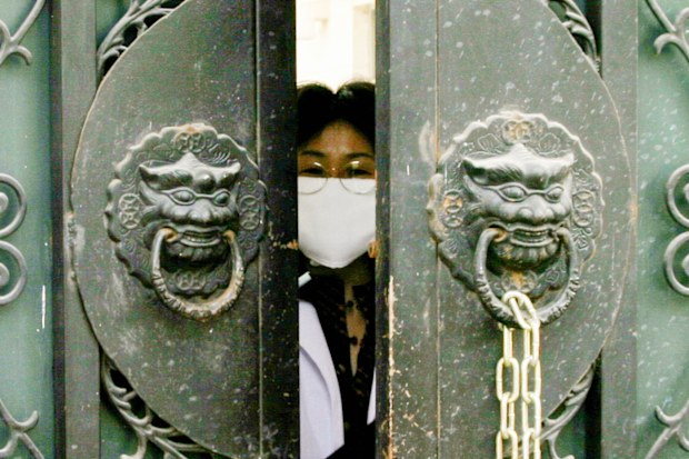 In this 2004 photo, a quarantined medical worker, wearing a face mask to protect against the Severe Acute Respiratory Syndrome (SARS) virus, peeks out of the entrance gate of the national institute of virology to pick up clothes and lunch boxes in Beijing, China.
