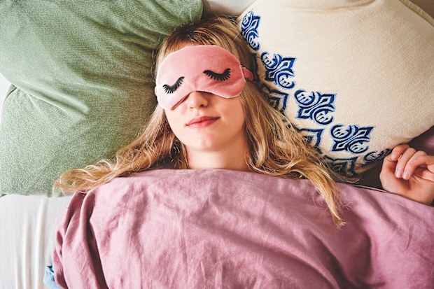 Young woman lying in bed and wearing a sleep mask 