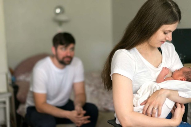 Mum breastfeeding while dad sits in left corner.