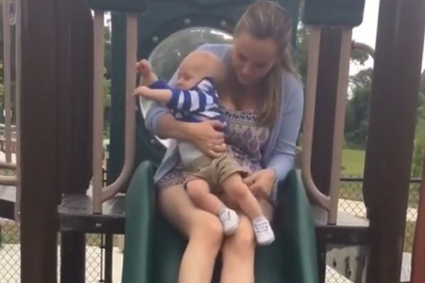 Mum riding down slide with baby in lap.
