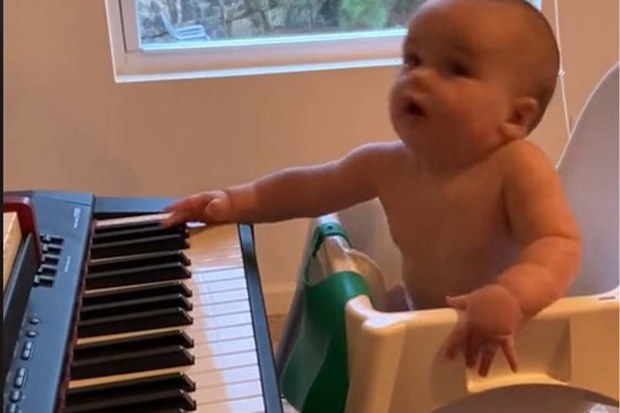 Baby moving his head along to music, sitting in front of a piano that his dad is playing.