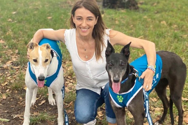 Dr. Katrina kneeling down hugging two greyhounds on either side of her.