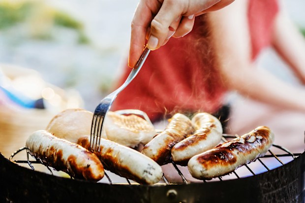 A close up of sausages being cooked on a barbecue by the lake.