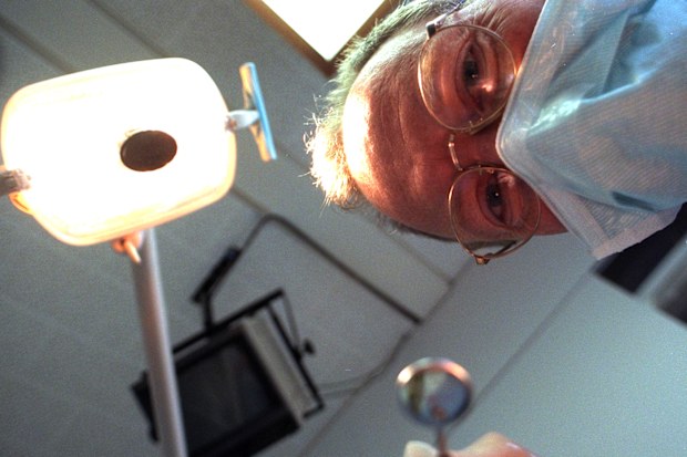 A dentist in a mask leans over a patient while carrying out dental work.