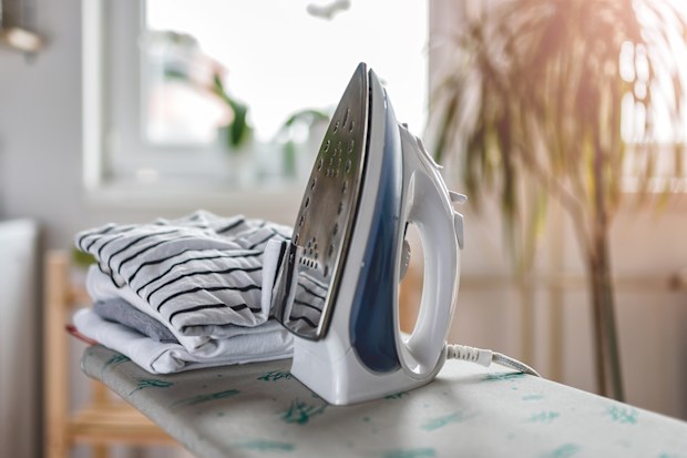Iron and cloth on ironing board at laundry room with washing machine visible in the background