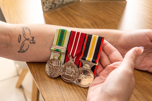 Mia Douglas holds her dad's ADF medals next to a tattoo she has in his honour.