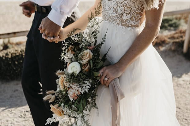 A close-up of bride and groom walking on path at the coast