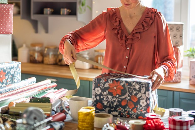 Woman wrapping gifts for Christmas at home on kitchen counter.