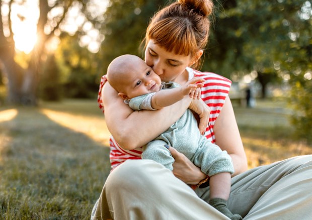 Mother and baby embracing while sitting down in meadow in sunset.