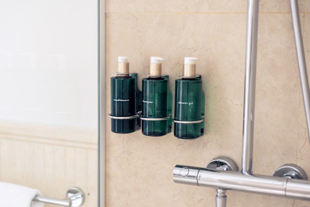 Modern bathroom interior featuring a shiny stainless steel shower and neatly arranged shampoo, shower gel and conditioner bottles. Clean design, hygiene and contemporary lifestyle concept