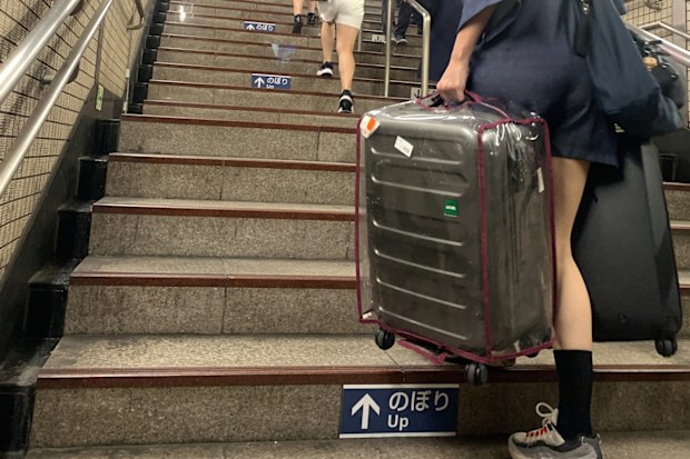 Tokyo, Japan - June 8, 2023: Asian tourists are having a hard time effort climbing the stairs because they carrying big heavy suitcases luggage from underground train station in Tokyo City when summer.