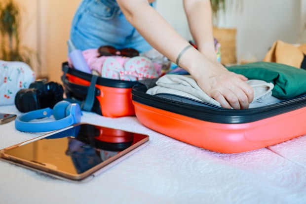 Travel packing, above and hands of a woman with clothes, holiday luggage and prepare for international summer. Suitcase, ready and person traveling with a suitcase, vacation clothing and hotel bag