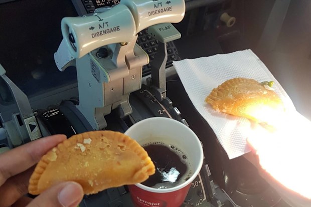 Two pilots drinking coffee and eating in their cockpit.