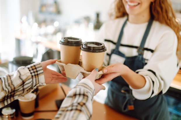 Smiling barista girl giving take away coffee cups to a customers.