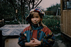 Little girl wearing warm clothing is standing in the backyard and looking at camera. Vintage photo