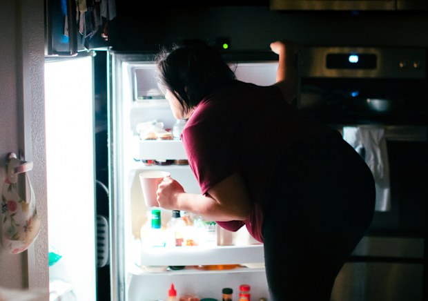 A pregnant woman is getting into the kitchen refrigerator at midnight to get a snack. Giving into her pregnancy cravings.
