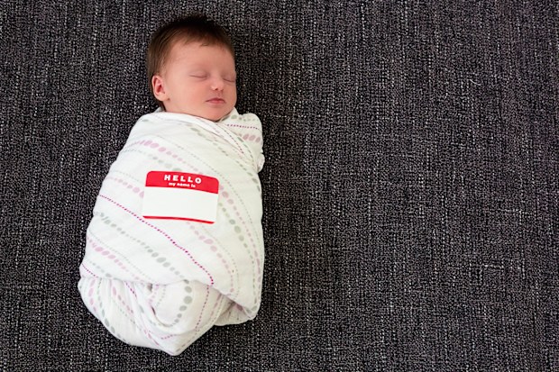 Sleeping swaddled infant with a "Hello my name is" sticker